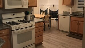 A kitchen with wooden cabinets, a microwave, stove, and a dining area with a table and chairs. - Beautifully Refurbished villa in an exciting active retirement community. (The Villages)