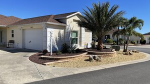 A single-story house with a garage, a landscaped front yard with a palm tree, and a clear blue sky. - Beautifully Refurbished villa in an exciting active retirement community. (The Villages)