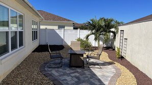 A patio area with a table and chairs, a small garden with pebbles and plants, and a white fence. - Beautifully Refurbished villa in an exciting active retirement community. (The Villages)