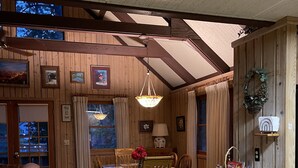 Un acogedor interior de cabaña con paredes de madera, una zona de comedor con mesa y sillas, y una cocina con armarios y cajones de madera.