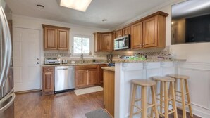 A kitchen with wooden cabinets, a microwave, a dishwasher, and a bar stool area. - Experience family fun at Turtle Time, a 4-bedroom home in Oak Island, NC. (Oak Island)