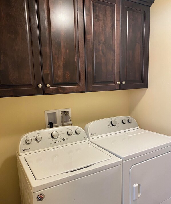 Un espace buanderie équipé de deux lave-linge et deux sèche-linge Whirlpool, avec des armoires en bois au-dessus et un mur blanc.