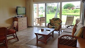 A room with a television, a dining table, chairs, a sofa, and a view of a garden through large sliding doors. - Kauai Pono Kai Resort BR/1BA Condominium -- Sleeps 4  (Kapaa)