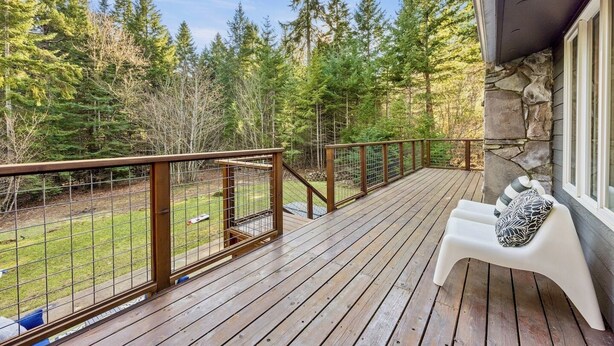 A wooden deck with a stone wall, a white bench, and a view of a forest. - Private 2.5 acres, Hot Tub, Fire Pit, Ping Pong, 10 minutes to town (Underwood)