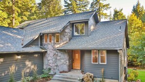 A two-story house with a stone facade, a front porch, and a well-maintained lawn. - Private 2.5 acres, Hot Tub, Fire Pit, Ping Pong, 10 minutes to town (Underwood)