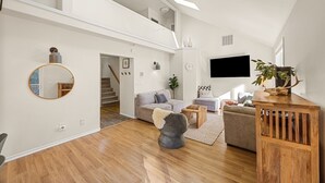 A spacious loft-style living area with a staircase, a large mirror, a flat-screen TV, and a wooden coffee table. - Private 2.5 acres, Hot Tub, Fire Pit, Ping Pong, 10 minutes to town (Underwood)