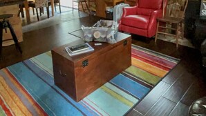 Interior acogedor de una cabaña de troncos con un comedor de madera, un sillón de cuero rojo, una chimenea y una alfombra colorida a rayas.