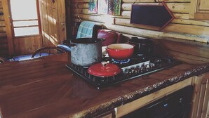 Una cocina rústica con paredes de madera, una estufa, ollas y una ventana.