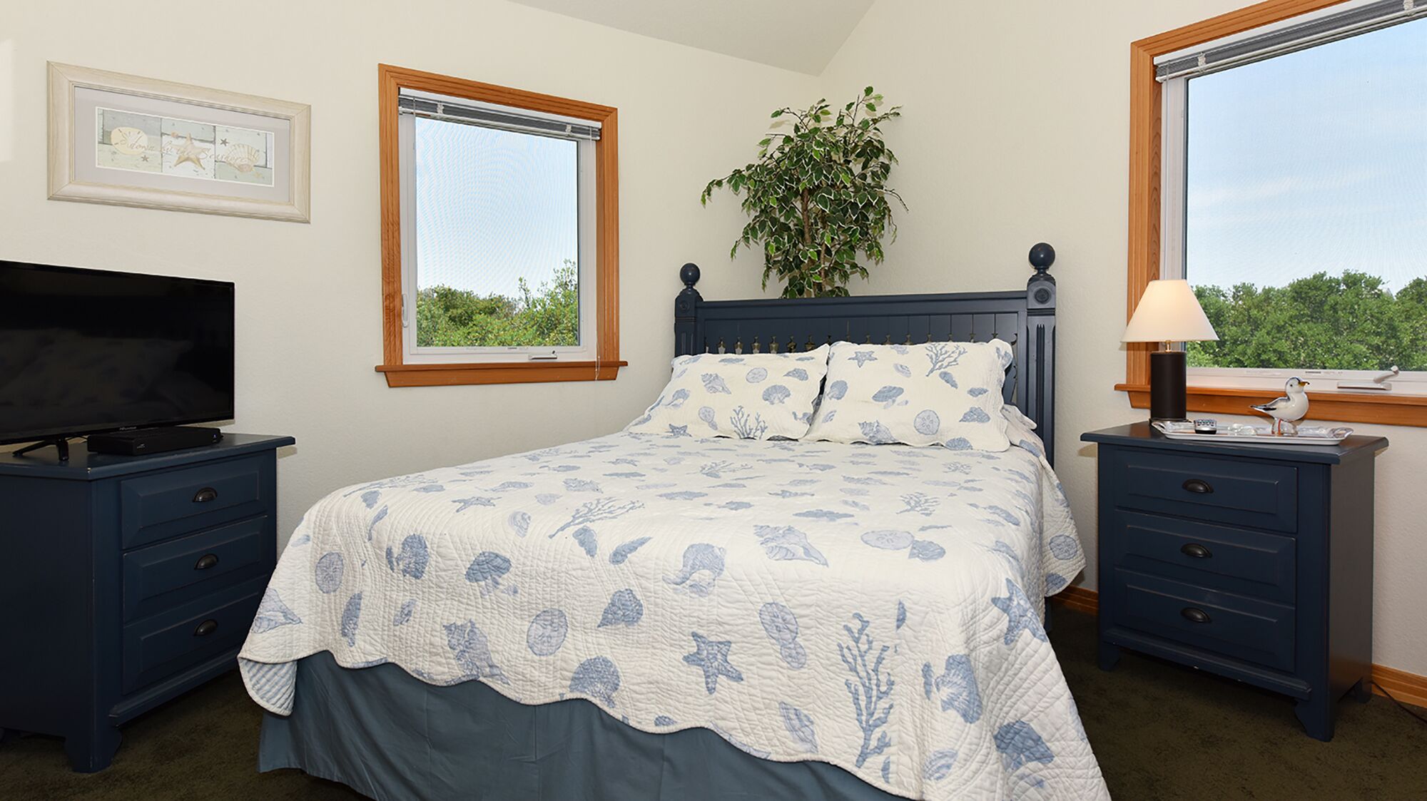 A bedroom with a bed, a TV, a nightstand, a lamp, and a window with a view of greenery.