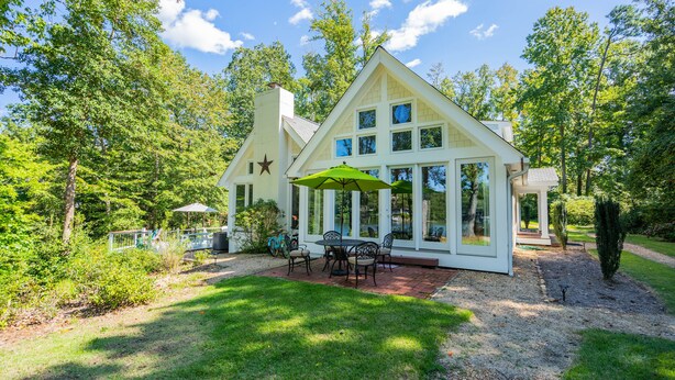 A house with a large patio, a dining area with outdoor furniture, and a view of the surrounding trees and landscape.