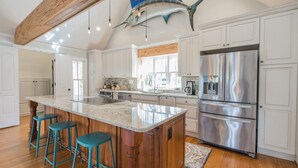 A spacious kitchen with white cabinetry, a large island with bar stools, a stainless steel refrigerator, and a ceiling with a wooden beam and a fish decoration.