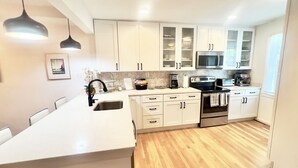 Een moderne keuken met witte kasten, een centraal eiland, roestvrijstalen apparatuur en hanglampen.