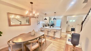 Een moderne keuken met een centraal eiland, hangende verlichting en een eethoek met een ronde tafel en barkrukken.
