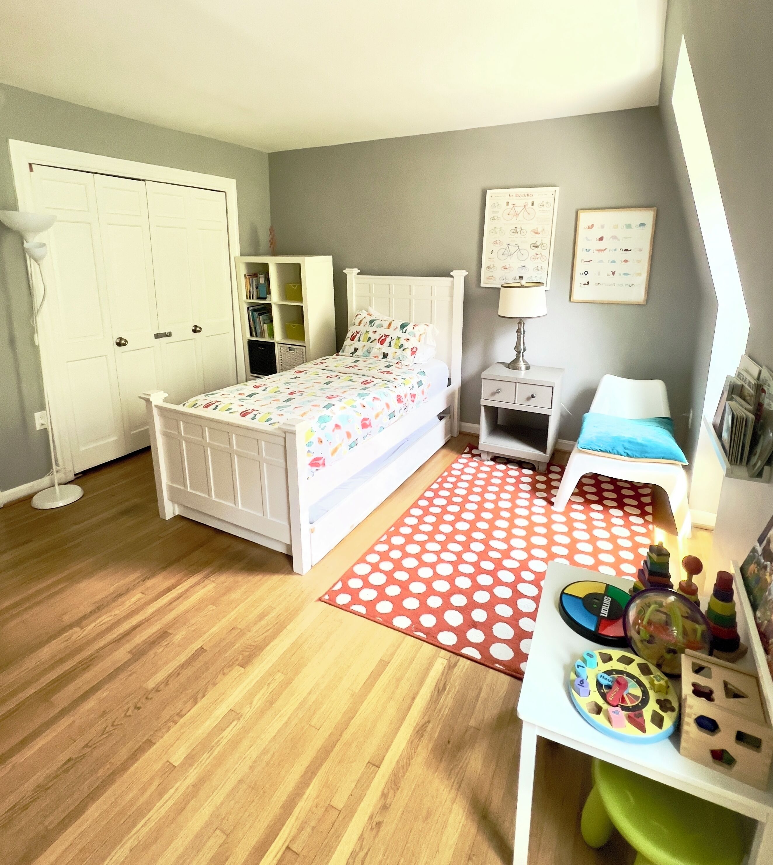 A bedroom with a bed, a desk with toys, a lamp, and a bookshelf.