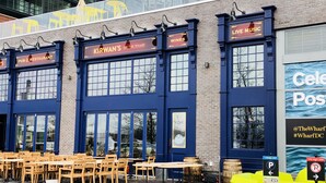 Een gebouw met een bord waarop 'Kirwan's Pub & Restaurant' en 'Live Muziek' staat, op de bovenverdieping. Er staan terrastafels en stoelen op het trottoir.