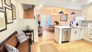 Een moderne keuken met witte kasten, een centraal eiland met een spoelbak en een eetgedeelte met een houten bank en gestreepte kussens.