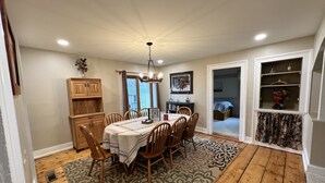 A dining area with a wooden table and chairs, a chandelier, and a patterned rug. - Private 150-Acre Farmhouse near Universities (Colton)