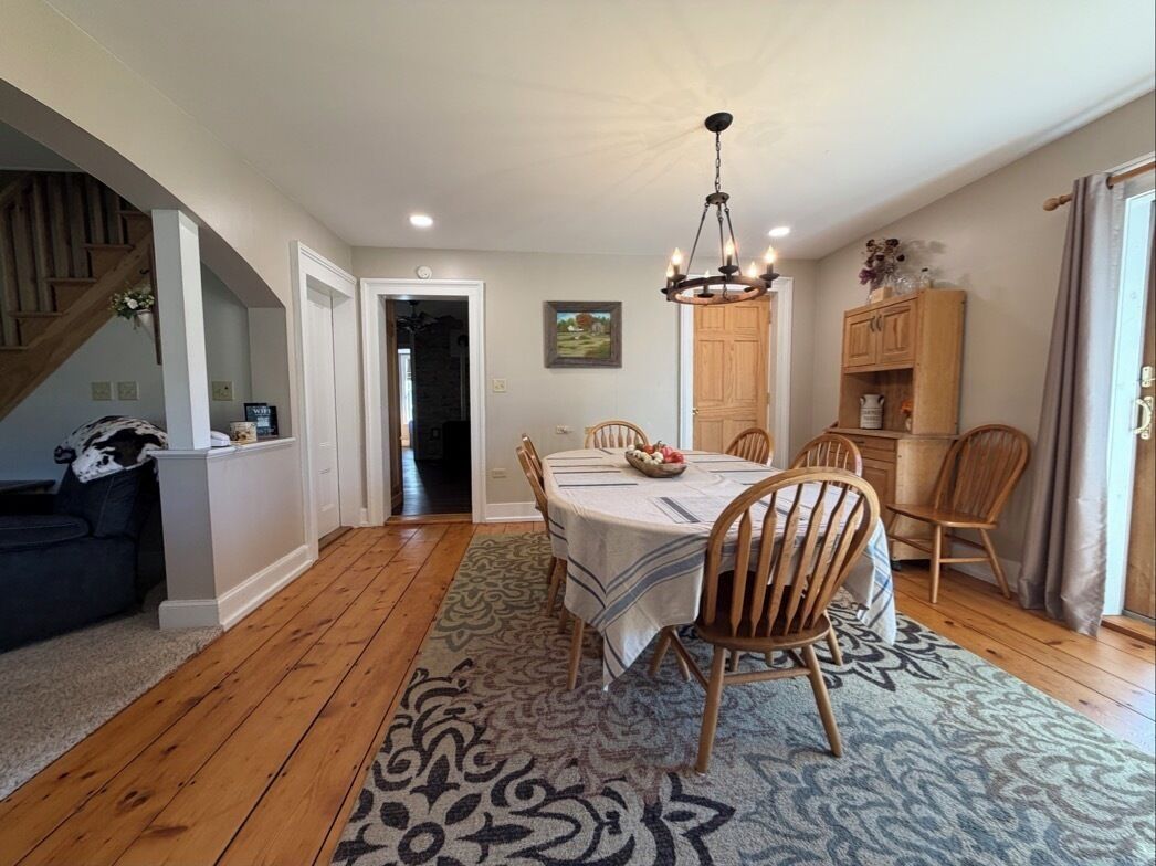 A dining area with a table set for six, surrounded by wooden chairs, a patterned rug, and a chandelier.
