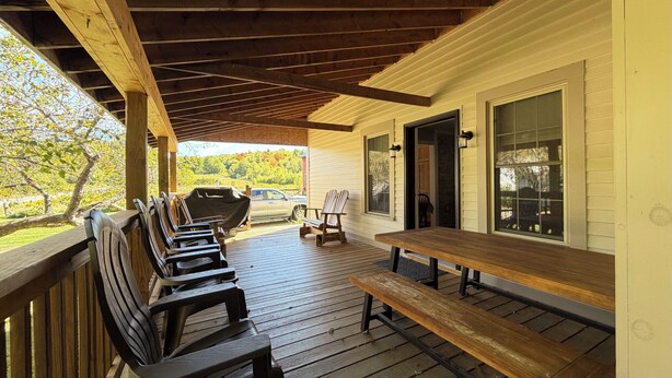 A covered outdoor area with wooden benches and picnic tables, a car, and a view of trees and a building. - Private 150-Acre Farmhouse near Universities (Colton)