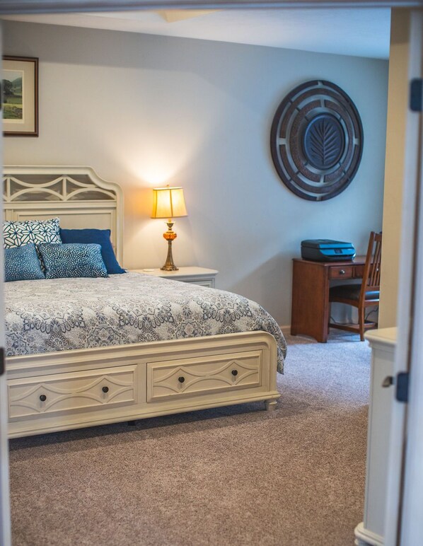 A bedroom with a bed, bedside table, lamp, and a wall decoration.