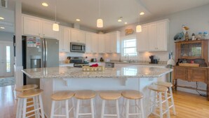 Une cuisine moderne avec des meubles blancs, des plans de travail en granit et des tabourets de bar.