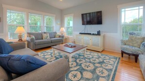 Un salon spacieux avec un canapé gris, un fauteuil bleu, une table basse en bois et un tapis à motifs.