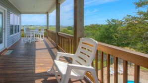 Une terrasse en bois avec des chaises blanches et une vue sur un paysage verdoyant.