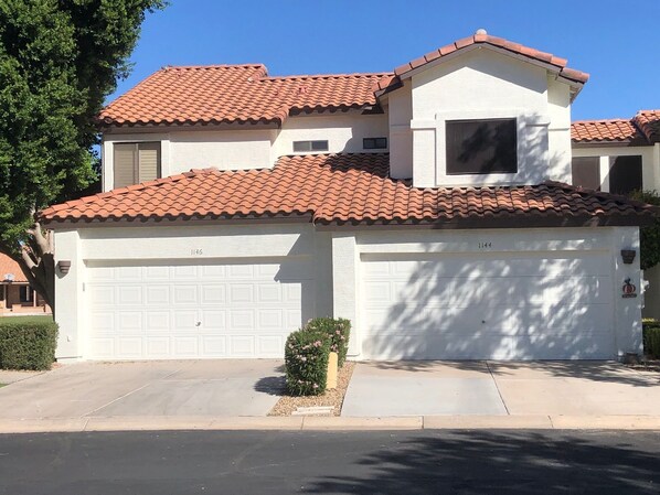 A two-story house with a red-tiled roof, a garage, and a small garden with pink flowers. - Beautifully Remodeled & Fully Furnished Townhouse on the Water! (Gilbert)