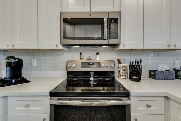 A kitchen with white cabinets, a stainless steel microwave, a gas stove, and a coffee maker. - Beautifully Remodeled & Fully Furnished Townhouse on the Water! (Gilbert)
