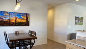 A dining area with a wooden table and chairs, a painting of a sunset, and a kitchen area with a countertop and cabinets. - Nestled in the Superstition Mountains! Amazing views! (Apache Junction)