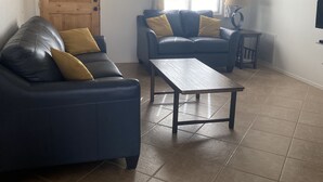 A living room with a dark blue sofa, a wooden coffee table, a ceiling fan, a wooden door, and a window with blinds. - Nestled in the Superstition Mountains! Amazing views! (Apache Junction)