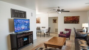 Un salon comprenant un téléviseur, un canapé en cuir, une table basse et un coin repas avec des chaises et une table.