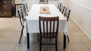 Un coin repas avec une table blanche, des chaises en bois, un lustre et une fenêtre avec des rideaux.