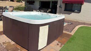Un bain à remous dans un jardin, avec un espace patio, un barbecue couvert et un auvent rouge.
