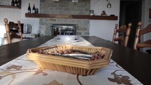 Une table à manger avec un panier de noix et une pince, un mur en pierre, une cheminée et des chaises en bois.