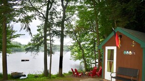 A cabin with a dock, red Adirondack chairs, a bench, and a view of a lake.