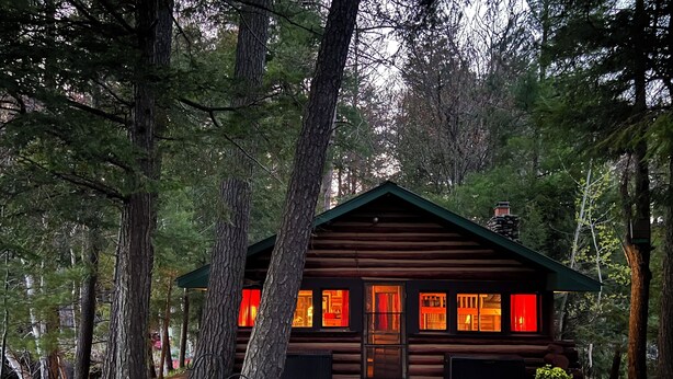 A log cabin with a wooden deck, surrounded by trees.