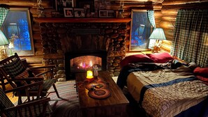 A cozy cabin interior with a stone fireplace, wooden furniture, and a bed with a quilt.