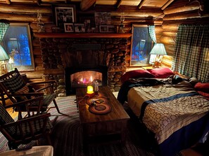 Interior acogedor de una cabaña con chimenea de piedra, muebles de madera y una cama con colcha.