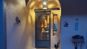 Un couloir avec une porte donnant sur une pièce, un panneau d’accueil et une plante en pot.