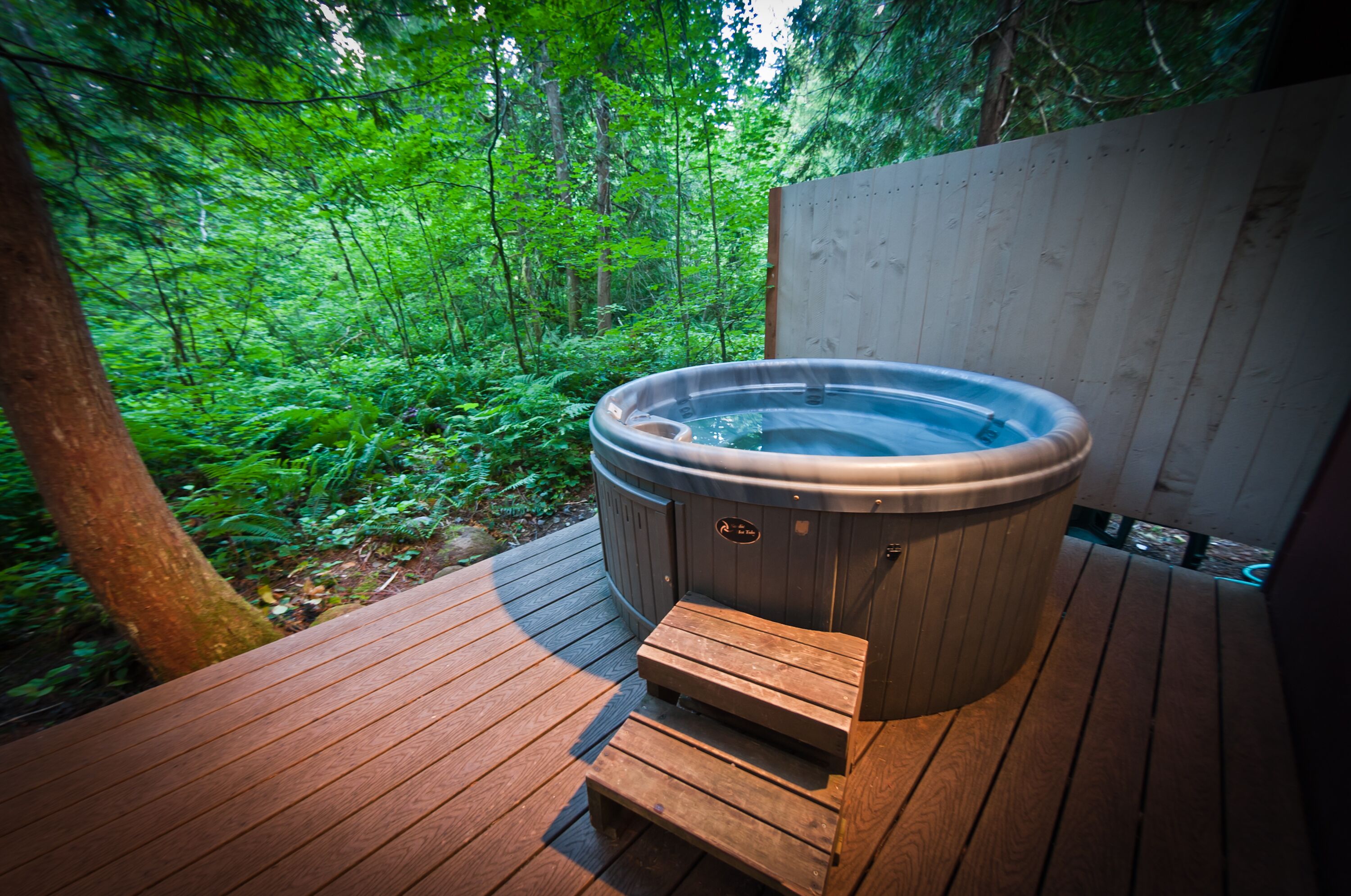 Ein Whirlpool auf einer Holzterrasse, umgeben von üppiger Vegetation.