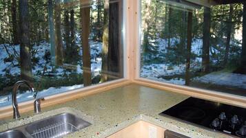 Una cocina con un amplio ventanal, un lavamanos de acero inoxidable y una placa de cocina negra.