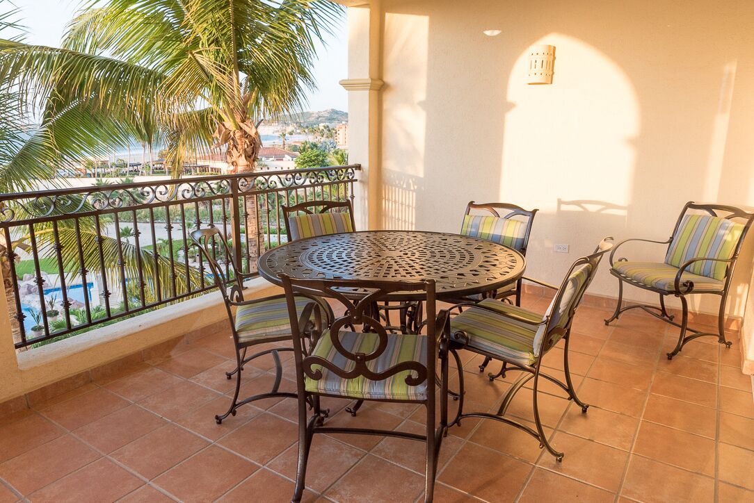 Un balcon avec une table ronde en métal et quatre chaises, chacune agrémentée de coussins à rayures.