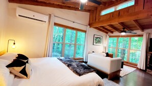 Un dormitorio amplio con una cama grande, una cama más pequeña y un sofá. Varias ventanas ofrecen luz natural y vistas al exterior.