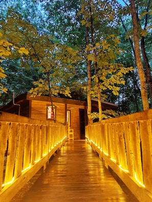 Un pont en bois, doté de rampes illuminées, mène à un bâtiment qui possède une porte et une enseigne.