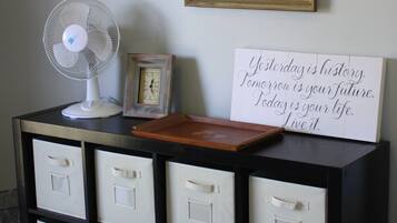 Une pièce comprenant un meuble de rangement noir, un ventilateur blanc, une horloge encadrée et une citation inspirante sur le mur.