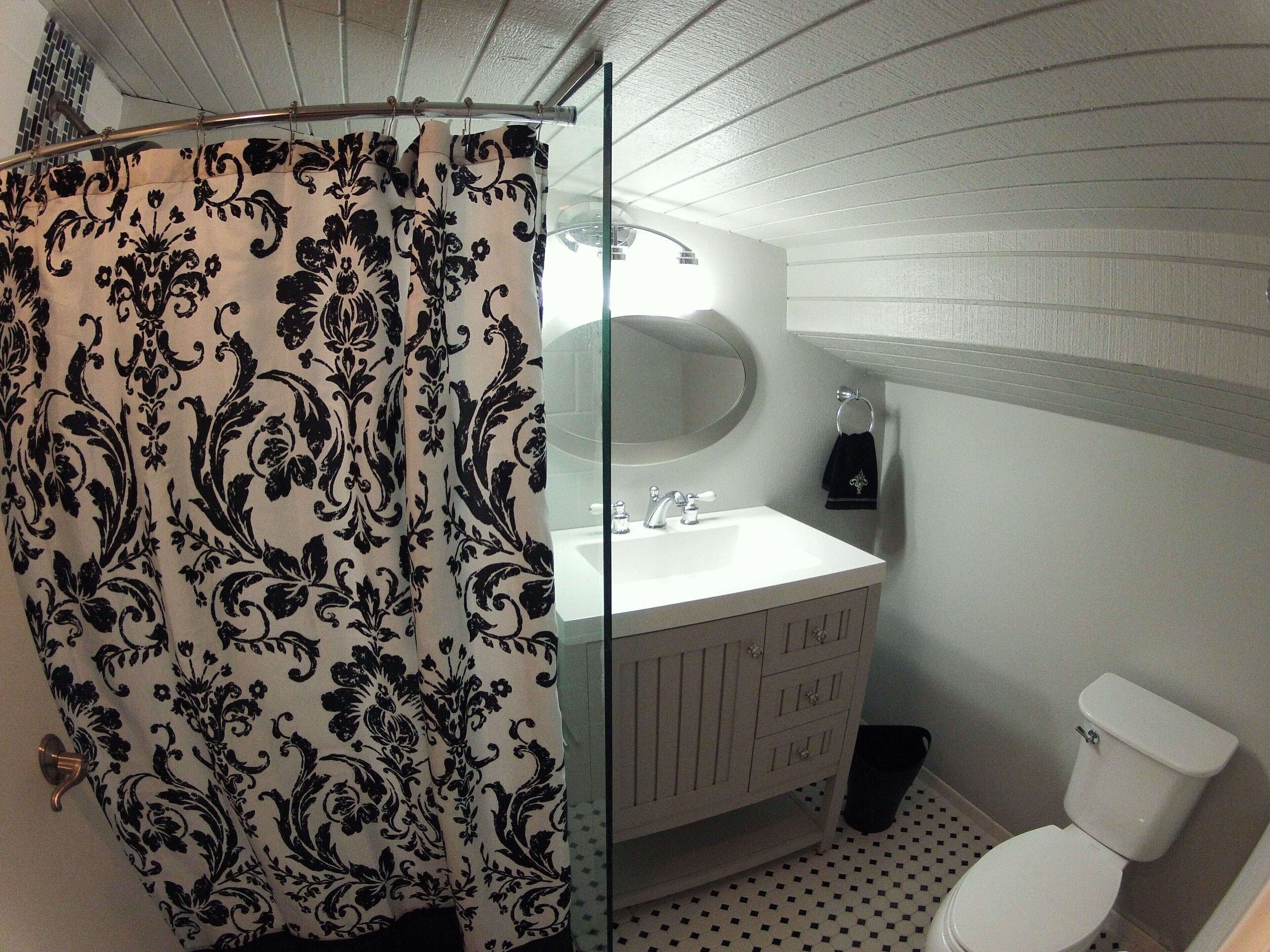 Et badeværelse med bruseforhæng, vask, spejl og toilet.