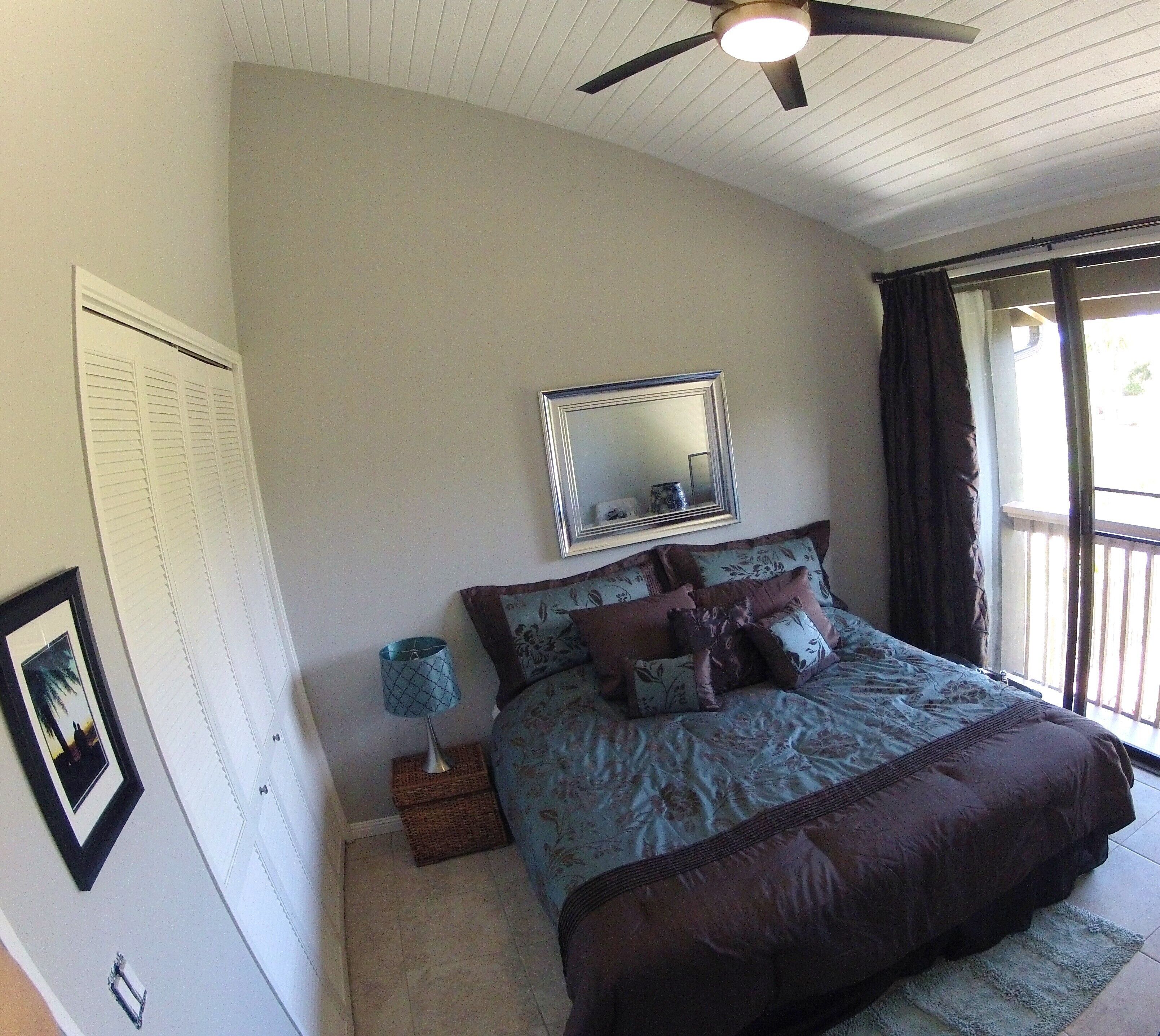 Ein Schlafzimmer mit Bett, Deckenventilator, Fenster und Spiegel.