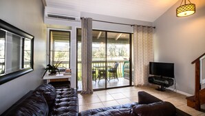 A living room with a sofa, a television, and a balcony with a table and chairs. - Comfortable Condo on Turtle Bay Golf Course Sleeps 5 (Kahuku)