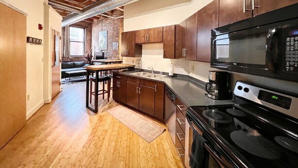 A modern kitchen with dark wooden cabinets, a black microwave, and a stainless steel stove. - Downtown Music City Loft living! ~Steps to the Ryman and Broadway. (Nashville)